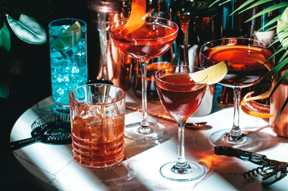 A set of cocktails with bottles on a marble table in a cosy, tropical-plants setting