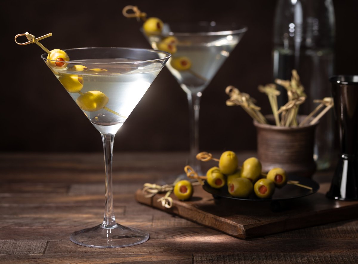 Martini cocktail with olives on bamboo picks in glass and bowl on dark wooden background