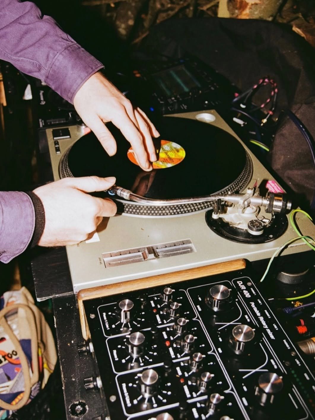 DJ with white gloves holding a vinyl record over a turntable and mixing equipment at a music setup