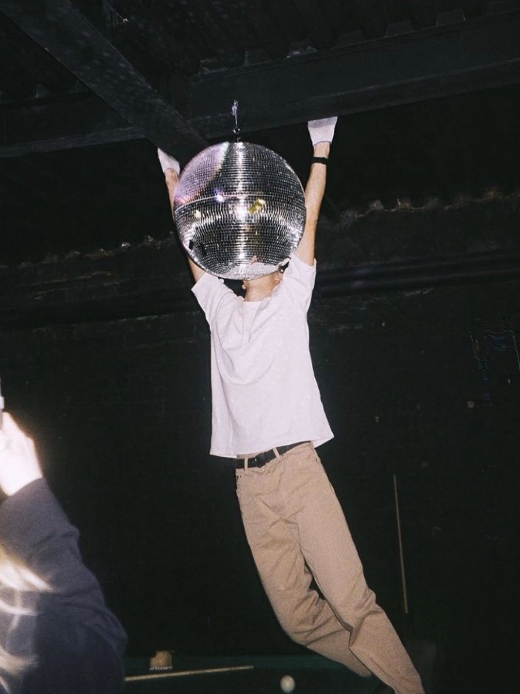 Person holding a large disco ball in front of their head at a nightclub venue